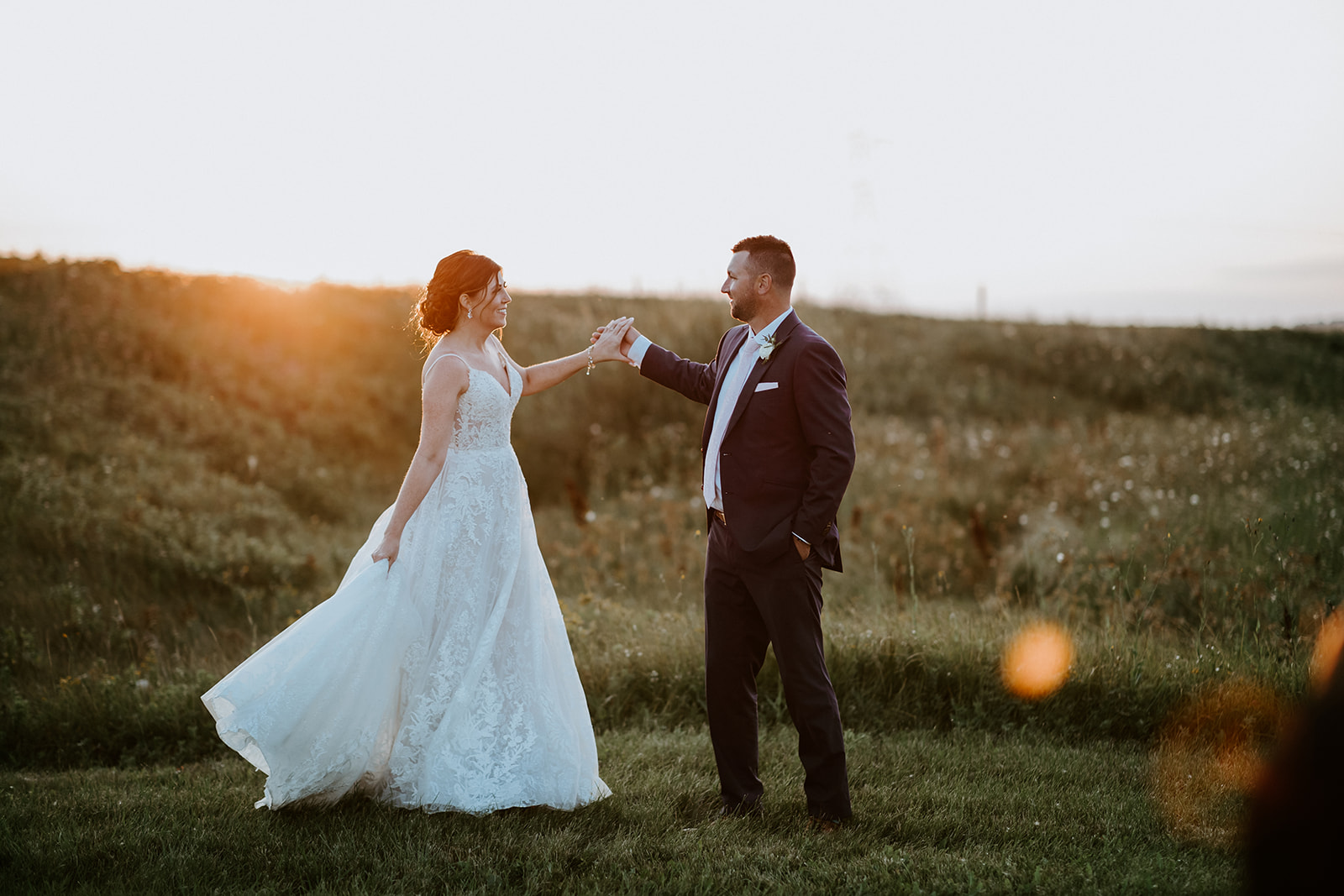 Bride and groom holding hands in a sunny field at dusk.