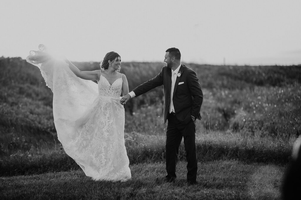 A bride and groom holding hands in a field, with the bride twirling her dress.