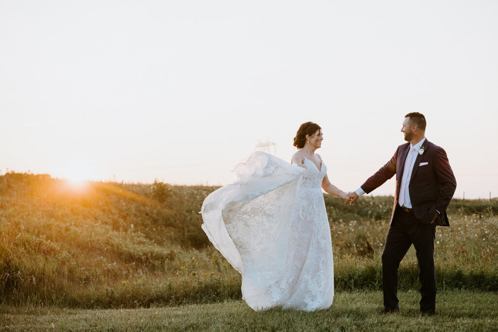Bride and groom holding hands in a field at sunset.