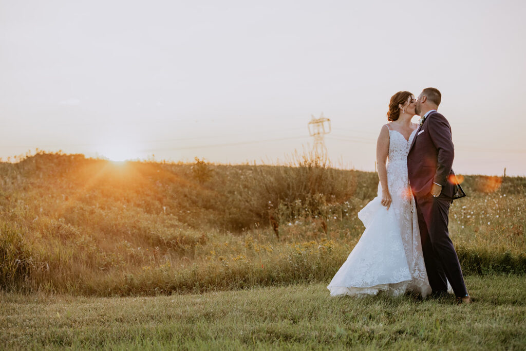 Bride and groom sharing a kiss in a field at sunset.