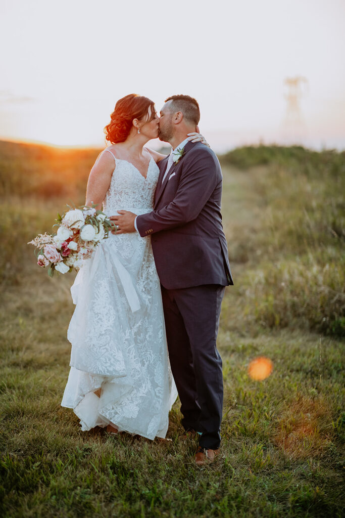 Bride and groom sharing a kiss in a field at sunset.