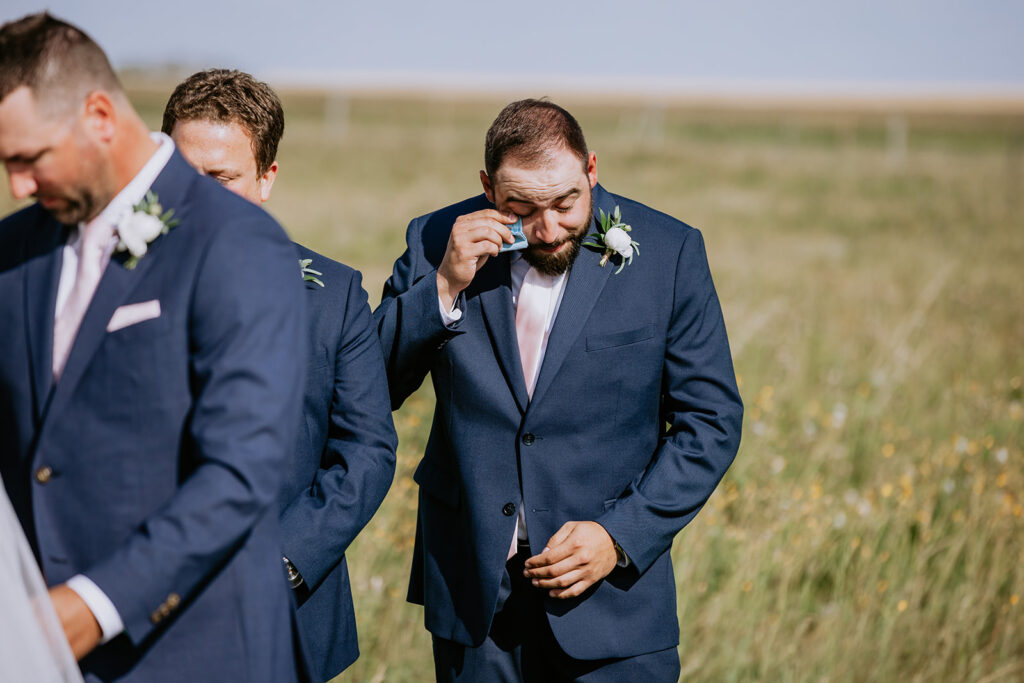 Groomsman wiping away a tear during an outdoor wedding ceremony.