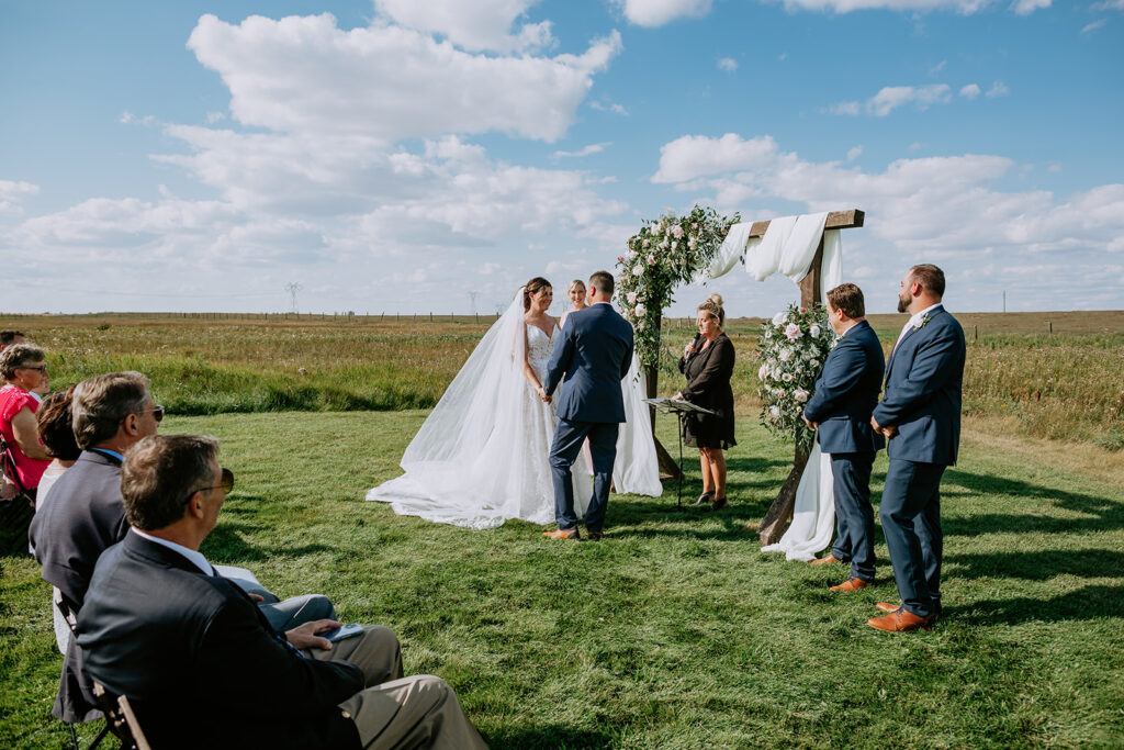 Outdoor wedding ceremony with bride and groom at the altar, guests seated in attendance on a sunny day.