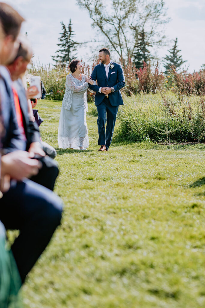 A bride and groom holding hands while walking down the aisle outdoors.