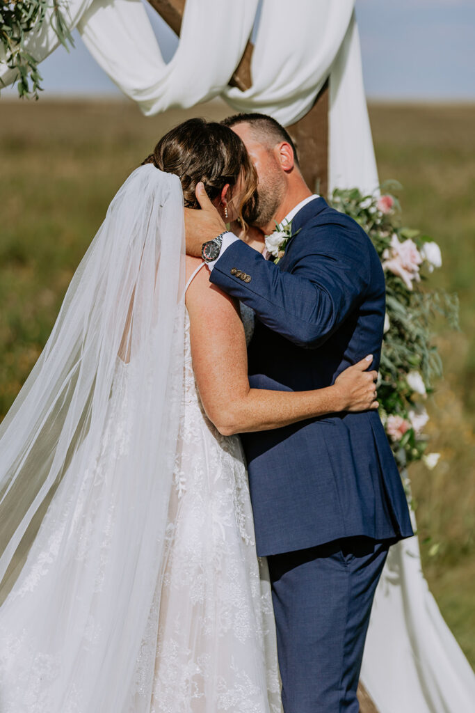 Bride and groom sharing an intimate kiss at their outdoor wedding ceremony.