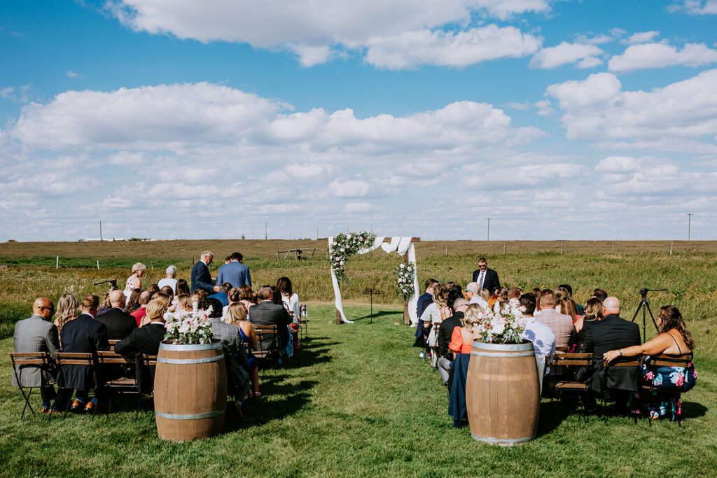 An outdoor wedding ceremony with guests seated on chairs arranged on a lawn before an altar under a clear blue sky.