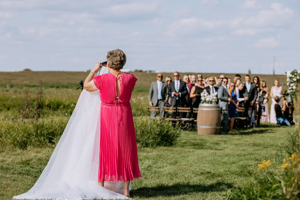 Woman in pink dress photographing a wedding ceremony outdoors.