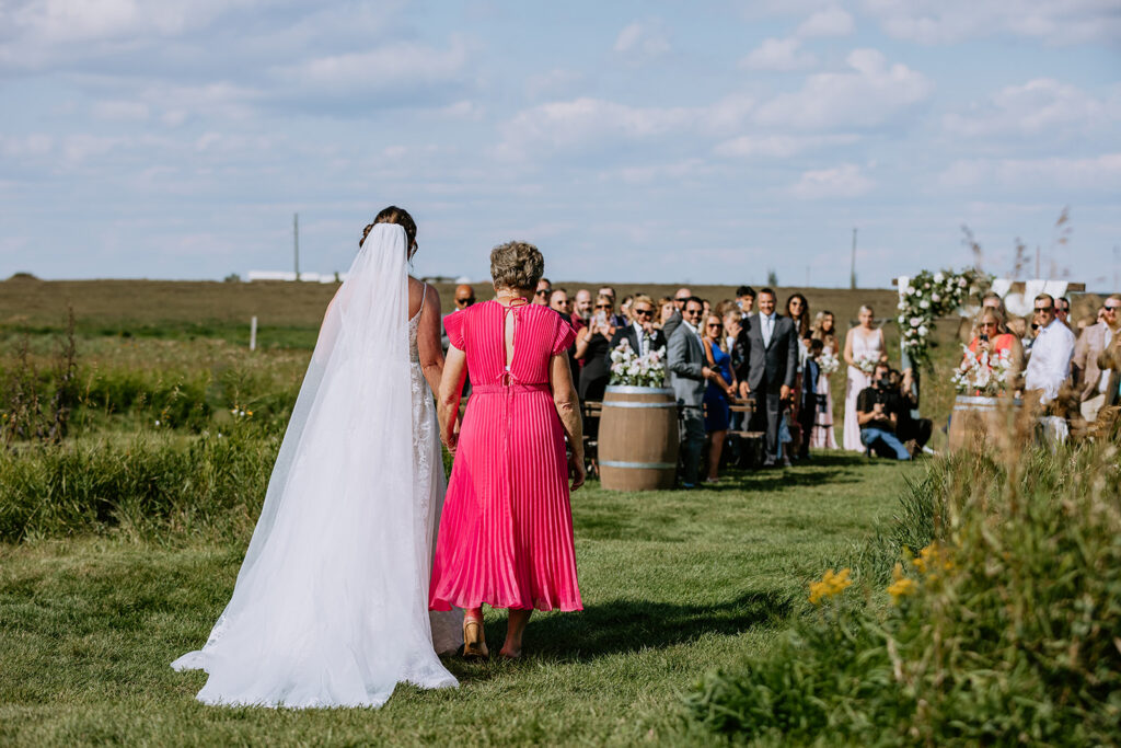 Bride walking towards an outdoor wedding ceremony with spectators looking on.