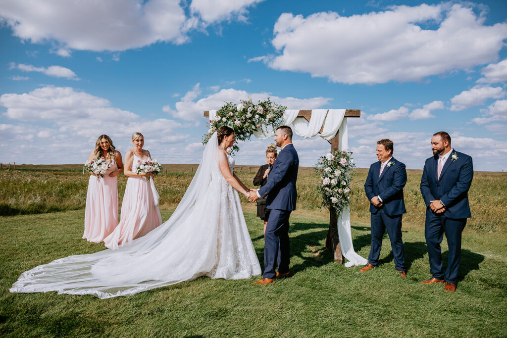 A wedding ceremony outdoors with a couple at the altar and a bridal party standing alongside.