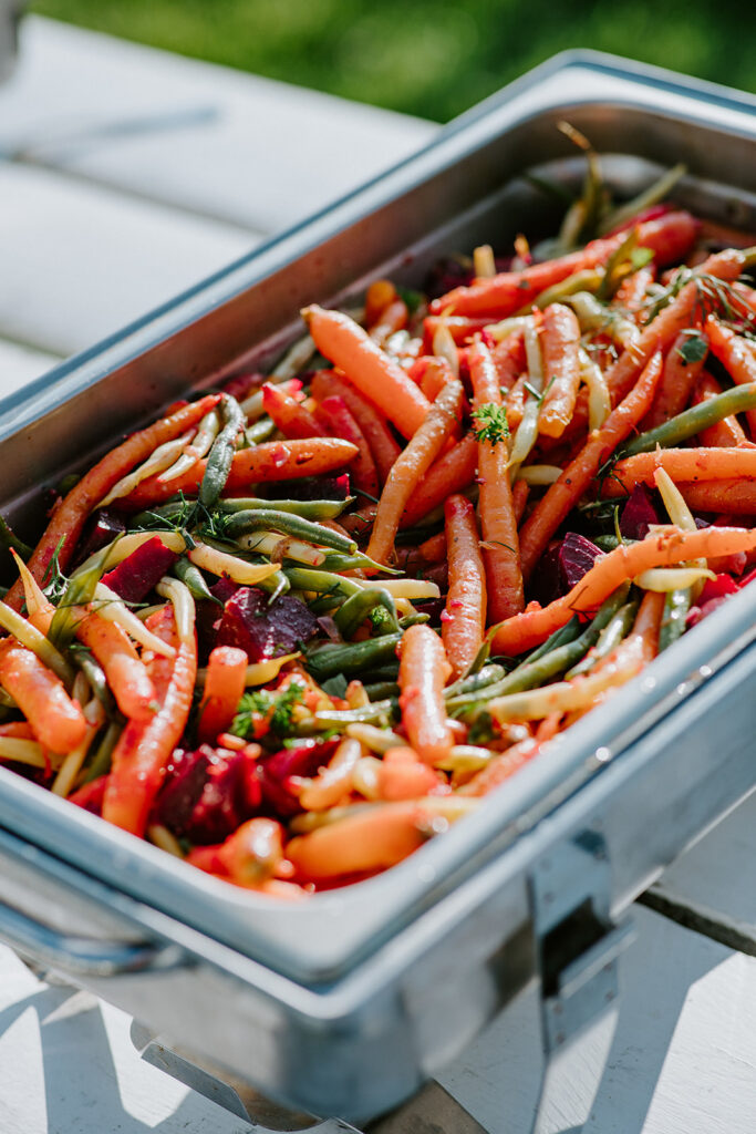 A tray of roasted carrots and mixed vegetables on a white wooden table.