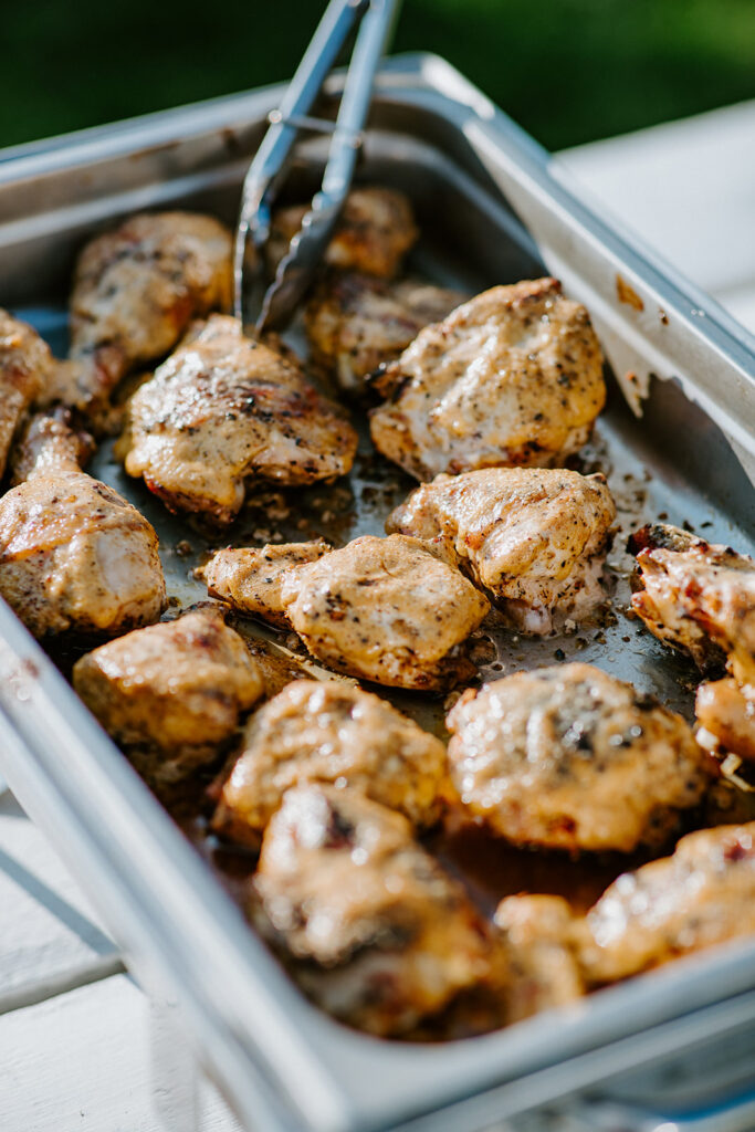 Grilled chicken thighs served in a metal tray with tongs.