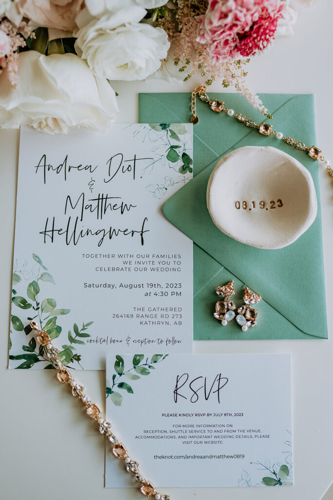 Elegant wedding invitation suite with floral design and gold jewelry accessories on a green background.