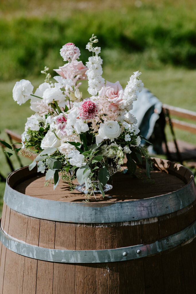 A floral arrangement featuring a mix of white and pink flowers displayed atop a wooden barrel.