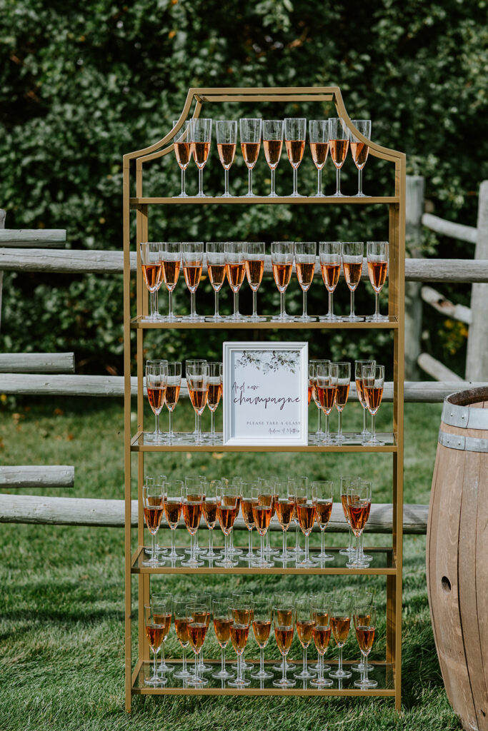 A champagne glass rack filled with glasses of rosé champagne next to a sign, set outdoors for an event.