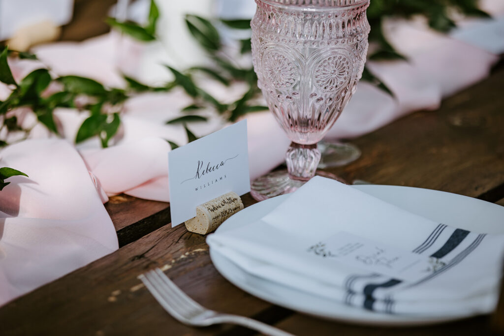 Elegant table setting with name card, pink glass, and decorative plate.