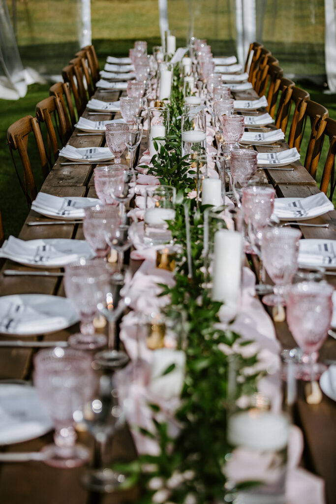 Elegantly set banquet table with greenery centerpiece and pink glassware.