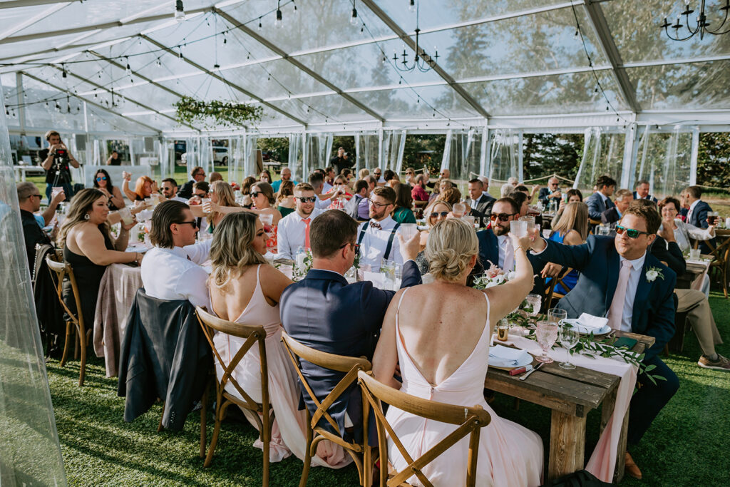 People toasting at a wedding reception under a clear tent.