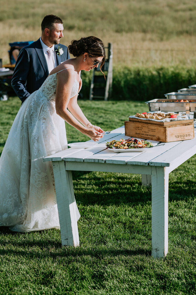 Bride and groom at a buffet table during an outdoor wedding reception.