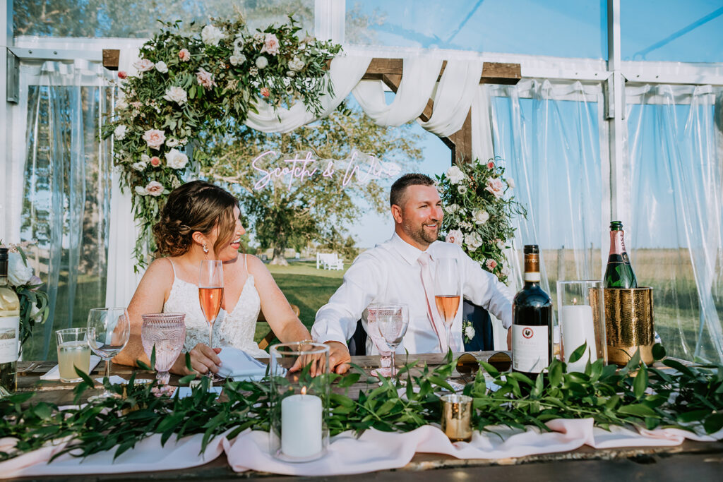 Couple seated at a decorated wedding table, laughing and enjoying a celebration.