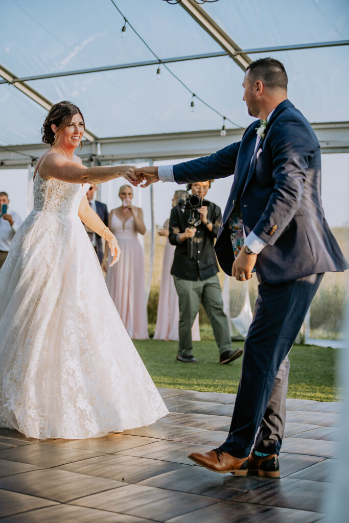 Bride and groom holding hands on the dance floor during an outdoor wedding ceremony.