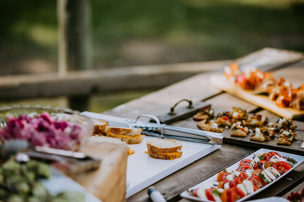 An outdoor buffet table set with a variety of appetizers and a focus on an artisan cheese board in the foreground.