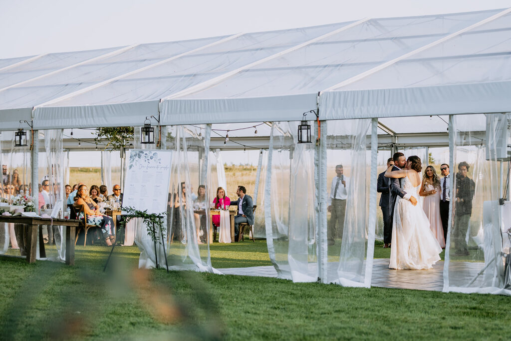 Wedding ceremony under a white tent with guests watching as the bride and groom embrace.