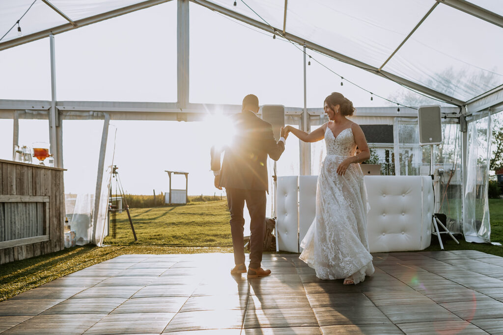 Bride and groom dancing under a tent with the sun setting in the background.