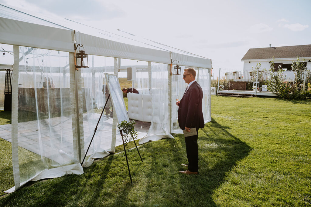 Man in a suit standing outside a white event tent on a sunny day.