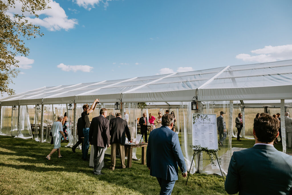 Guests mingling at an outdoor event under a white marquee tent on a sunny day.