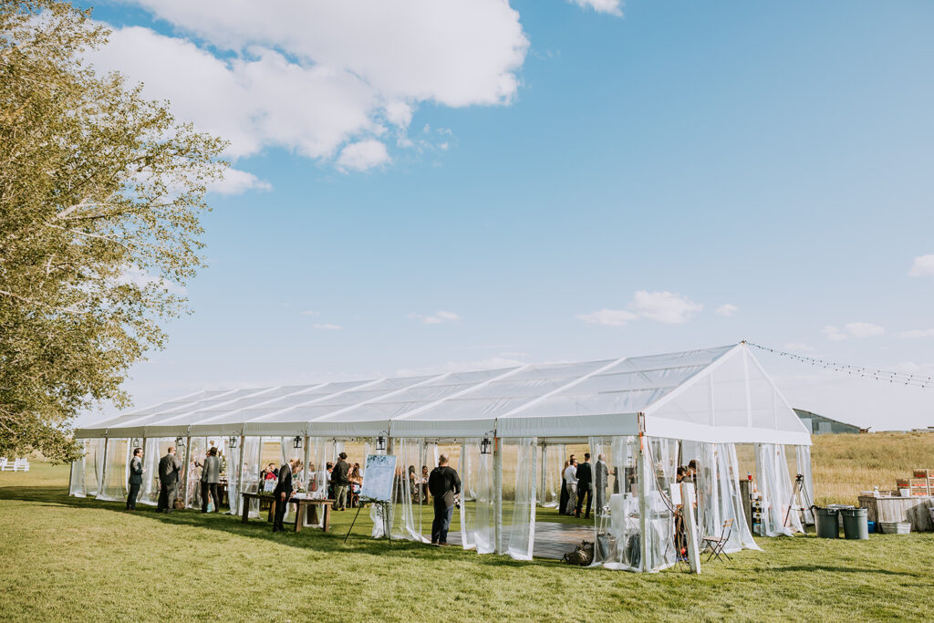 Outdoor event with guests under a large white tent on a sunny day.