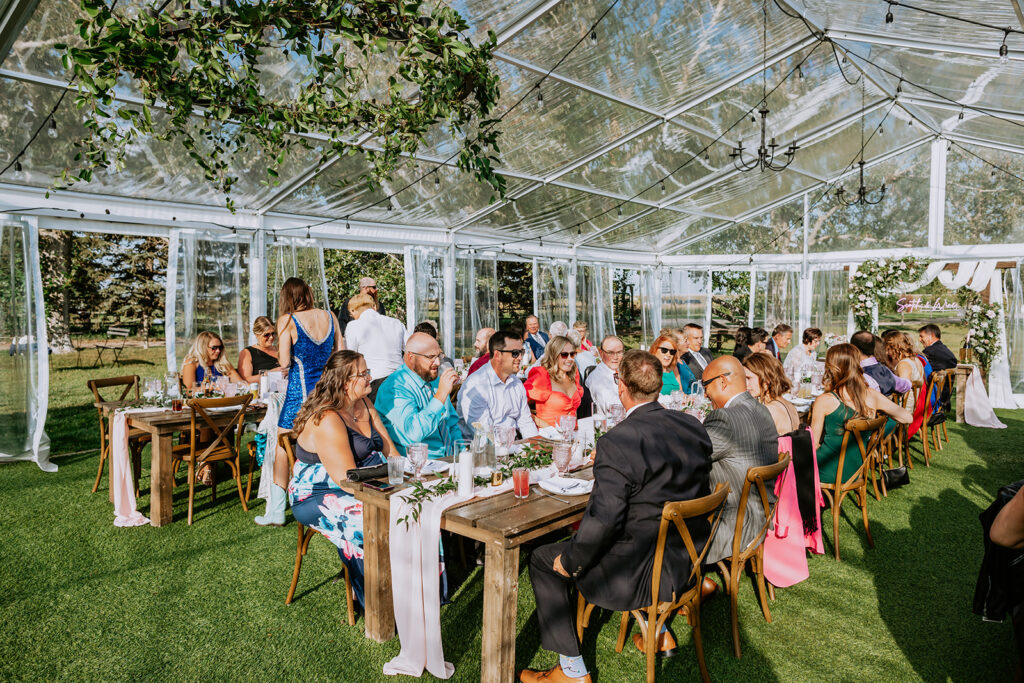 Guests seated at dinner tables during an outdoor event under a clear tent.