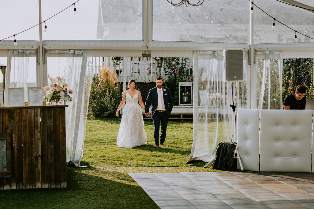 A couple holding hands and walking across a lawn at an outdoor wedding venue.