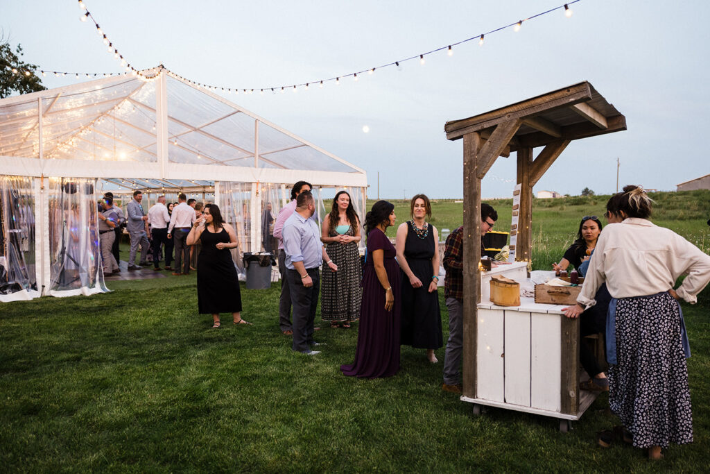 Guests mingling and queuing at a food stand during an outdoor evening event under string lights.