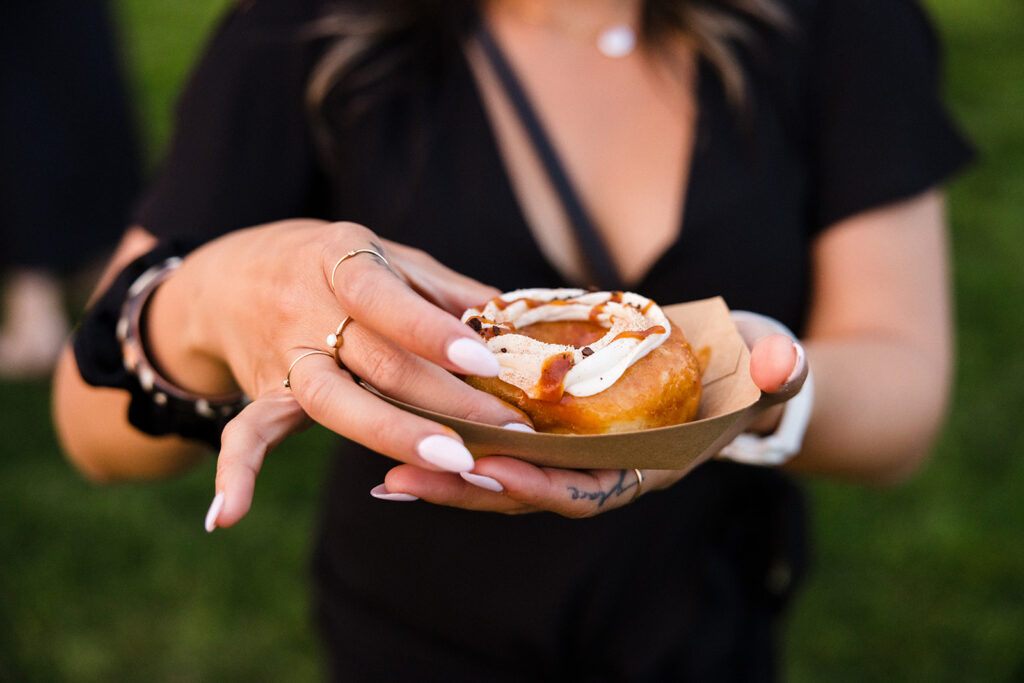 A person holding a cinnamon roll in a paper tray.