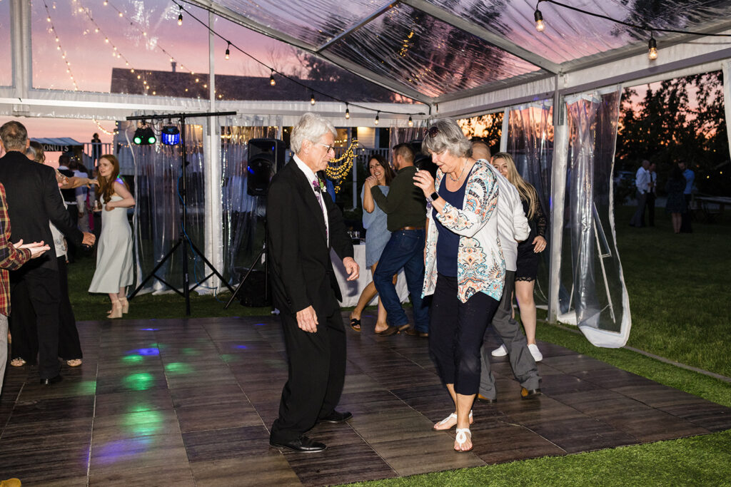 A couple dancing on a tent-covered dance floor at an evening outdoor event.