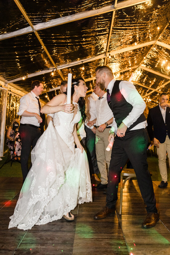 Bride and groom dancing with guests at a wedding reception under a canopy of lights.