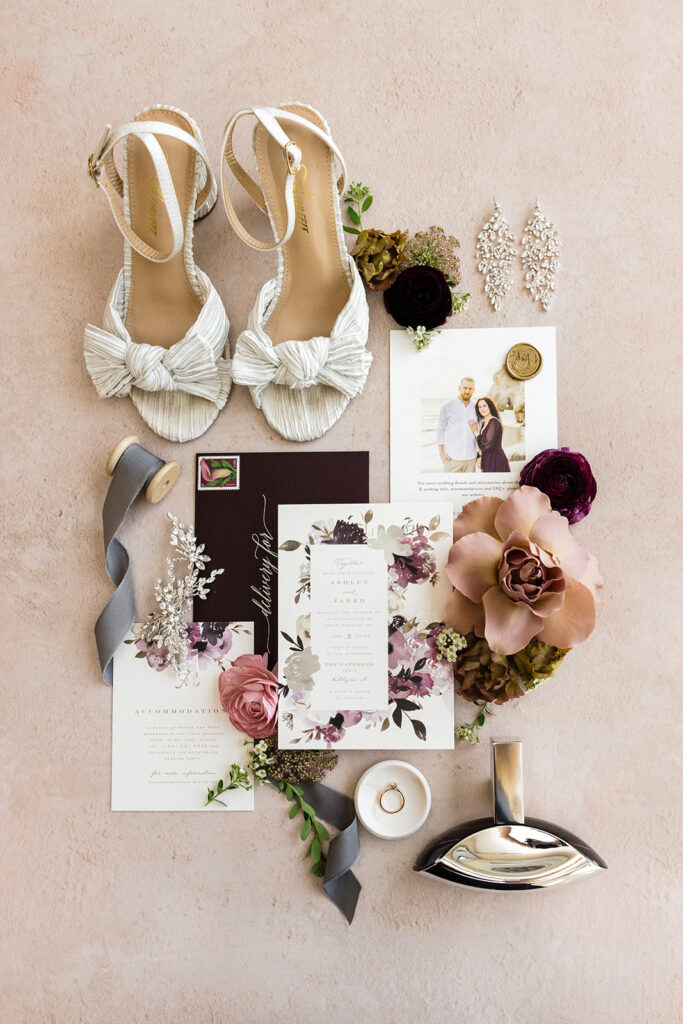 Flat lay of wedding accessories, including shoes, invitation, and jewelry with floral decorations.