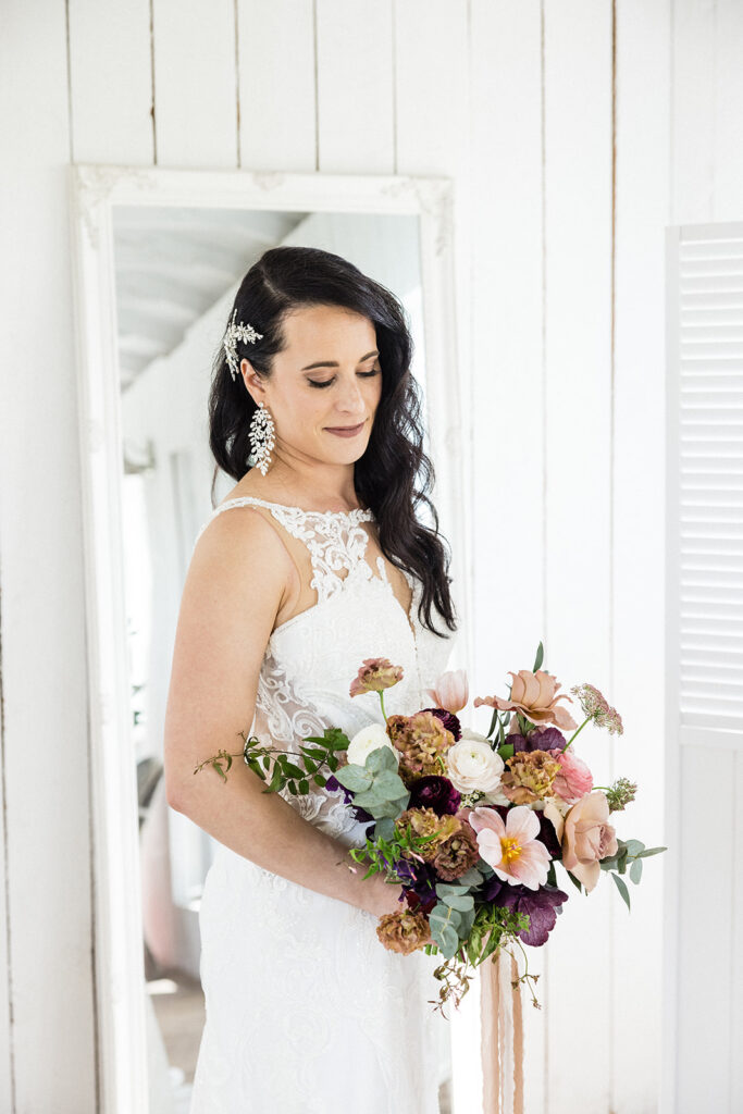 A bride in a white dress holding a bouquet of flowers. A Garden Wedding with Pops of Plum