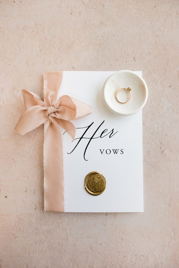 Elegant wedding vow booklet with a satin ribbon, engagement ring, and wax seal.
