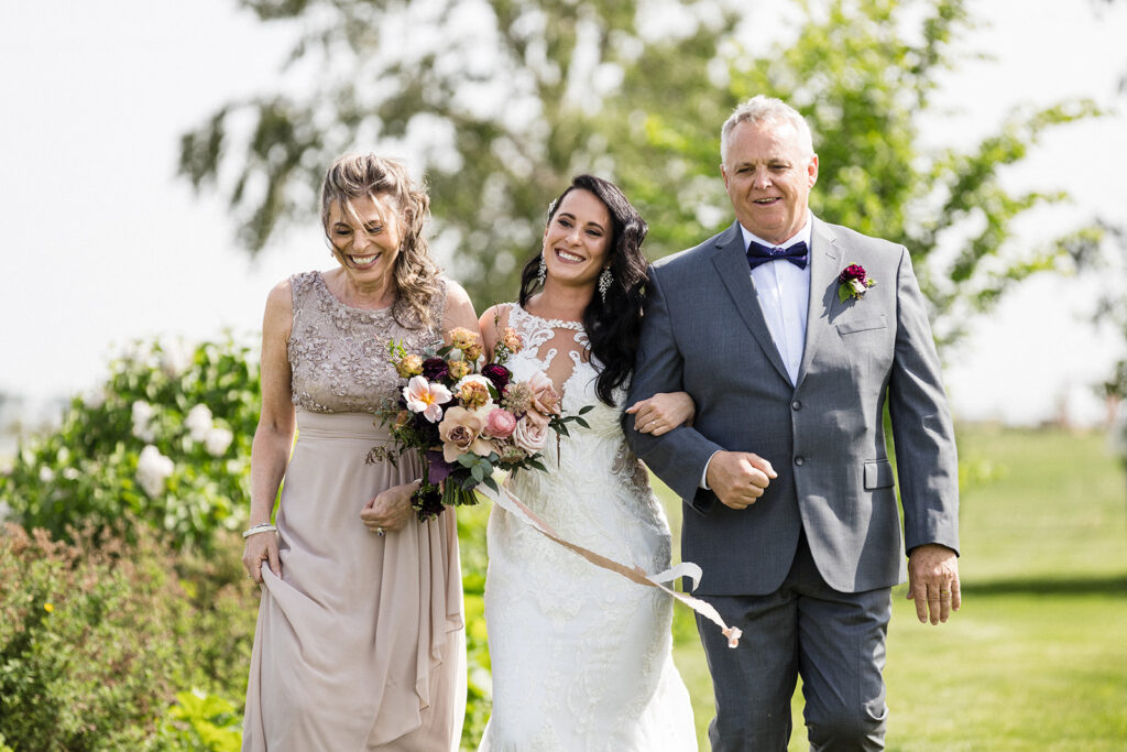A bride walks arm in arm with her parents on a sunny wedding day.