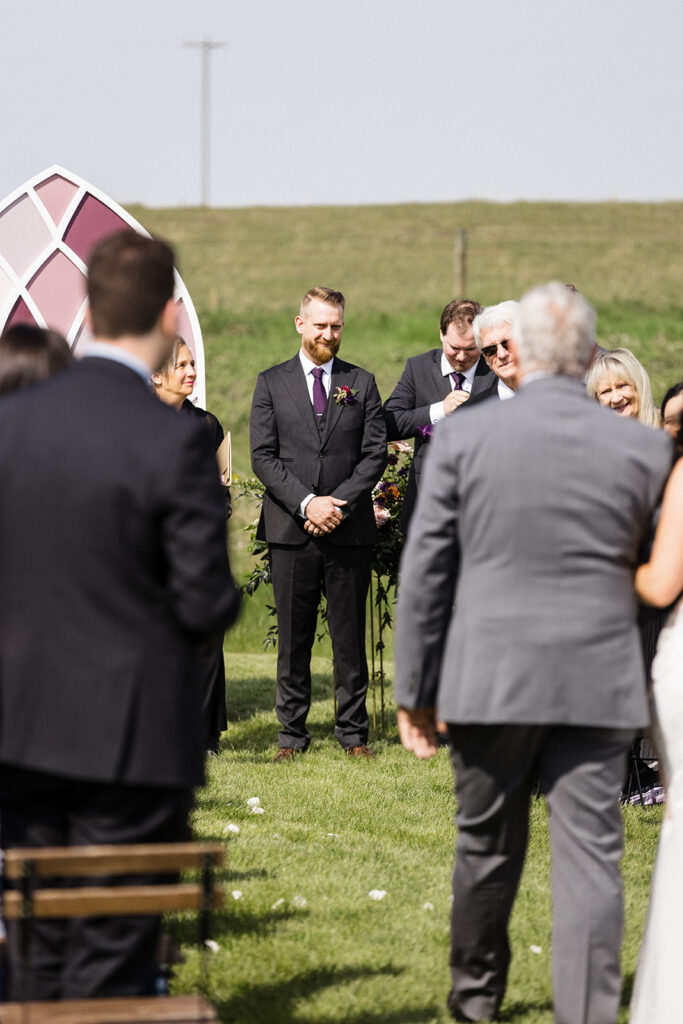 A groom waiting at the altar during an outdoor wedding ceremony.