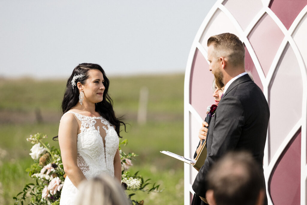 Bride and groom stand facing each other during an outdoor wedding ceremony.