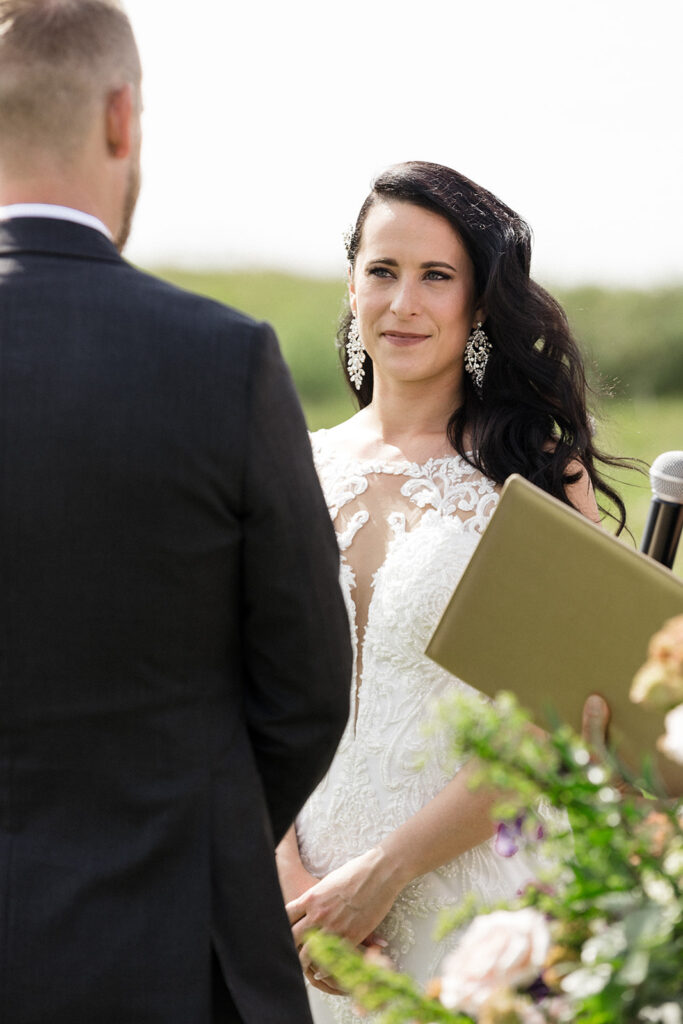 Bride exchanging vows with groom during outdoor wedding ceremony.