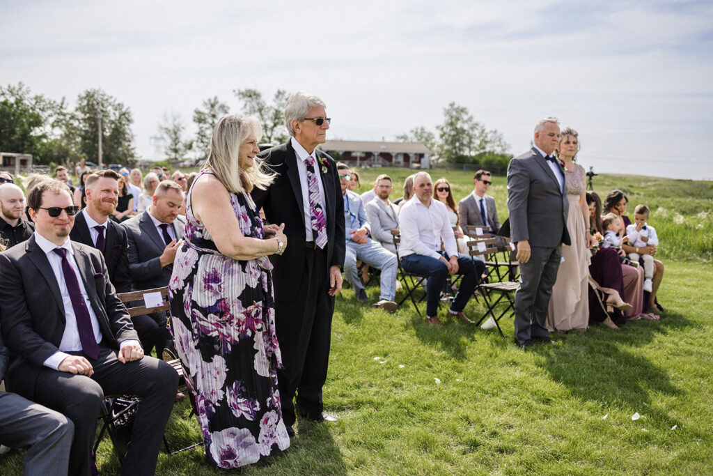 Guests standing and sitting at an outdoor wedding ceremony.