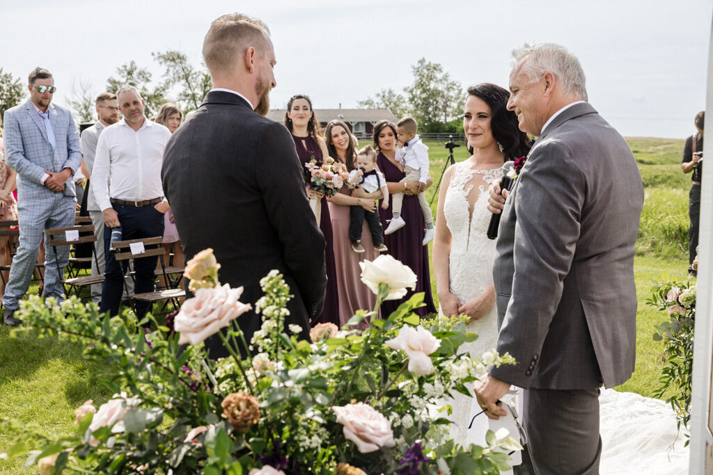 A bride walking down the aisle accompanied by an older gentleman, with guests looking on and the groom waiting at the altar.