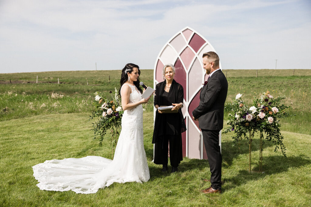 A couple exchanging vows at an outdoor wedding ceremony with an officiant standing between them.