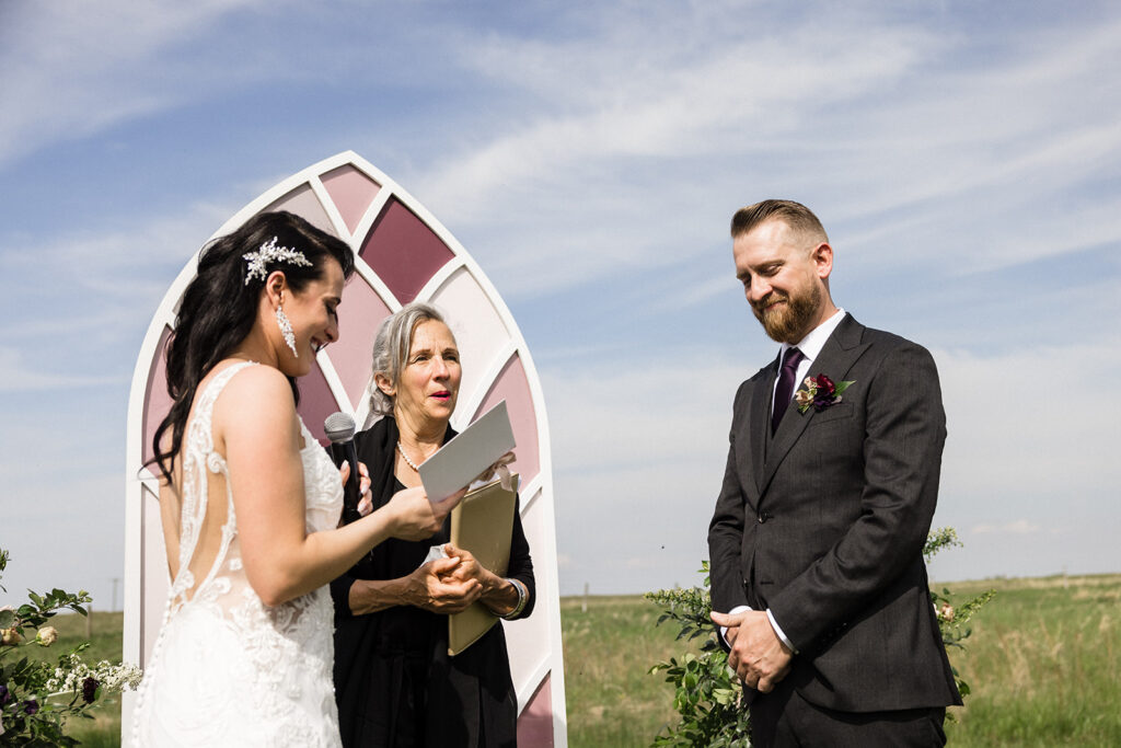 A bride and groom stand before an officiant at an outdoor wedding ceremony.