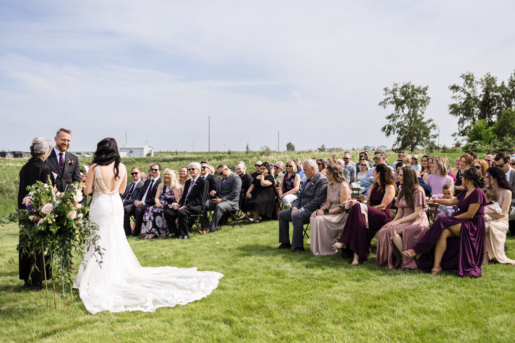 A bride and groom stand at the altar during an outdoor wedding ceremony with guests seated on either side.