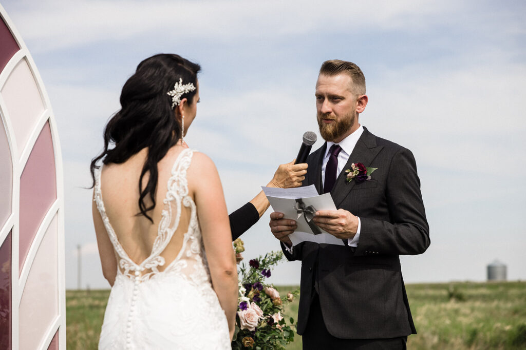 A groom reading his vows to a bride during an outdoor wedding ceremony.