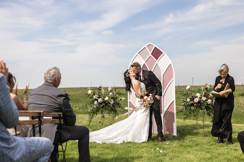 Bride and groom share a kiss at their outdoor wedding ceremony.